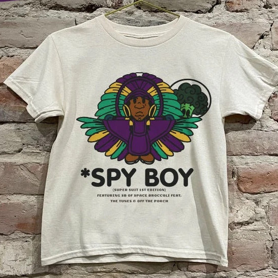 White mardi gras t-shirt with 'Spy Boy' graphic design hanging on a brick wall.