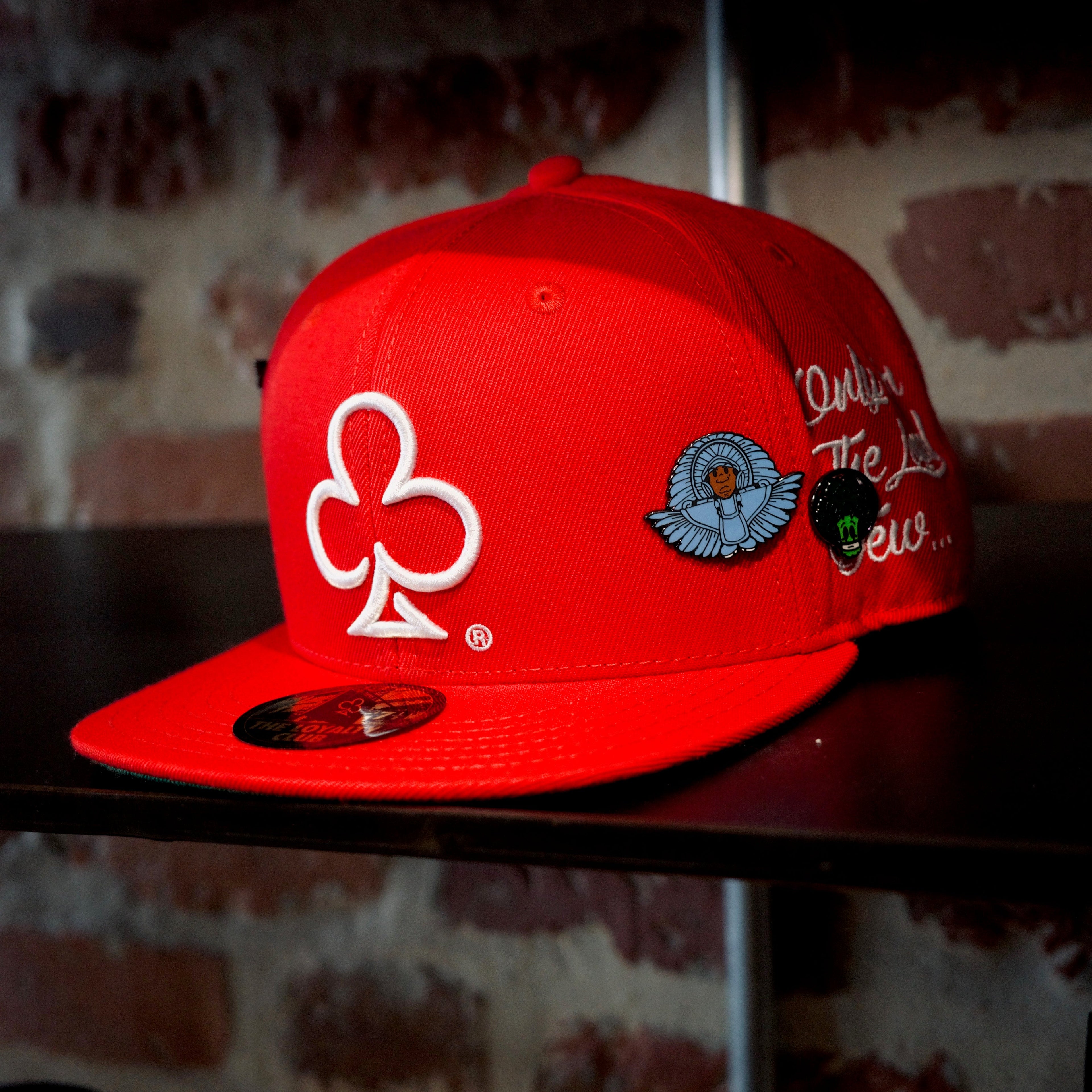 Red cap with embroidered loyalty club logo and spy boy space broccoli pins